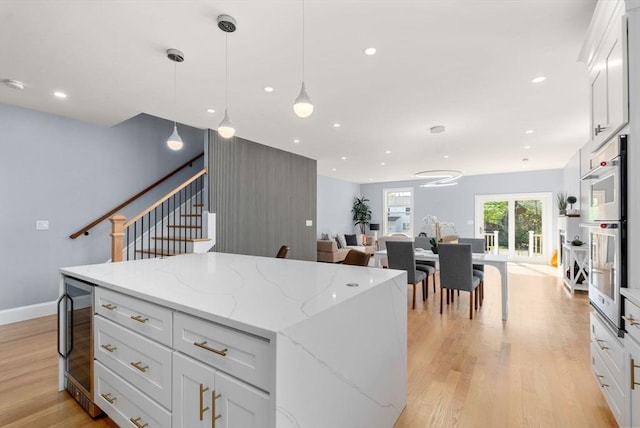 kitchen featuring white cabinets, a center island, open floor plan, light wood-type flooring, and wine cooler