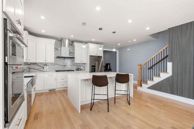 kitchen with decorative backsplash, appliances with stainless steel finishes, a center island, white cabinetry, and wall chimney exhaust hood