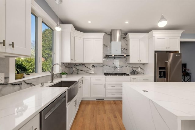 kitchen featuring decorative backsplash, white cabinetry, a sink, stainless steel appliances, and wall chimney exhaust hood