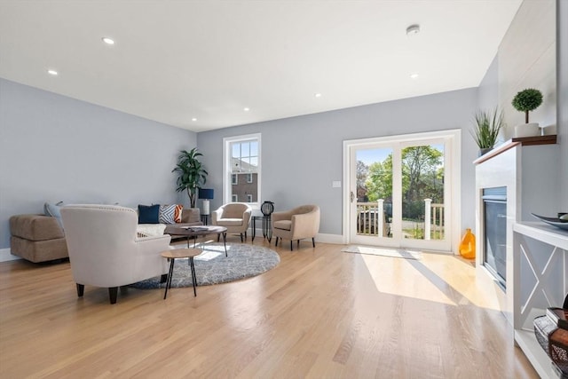 living room featuring recessed lighting, baseboards, a fireplace with flush hearth, and wood finished floors