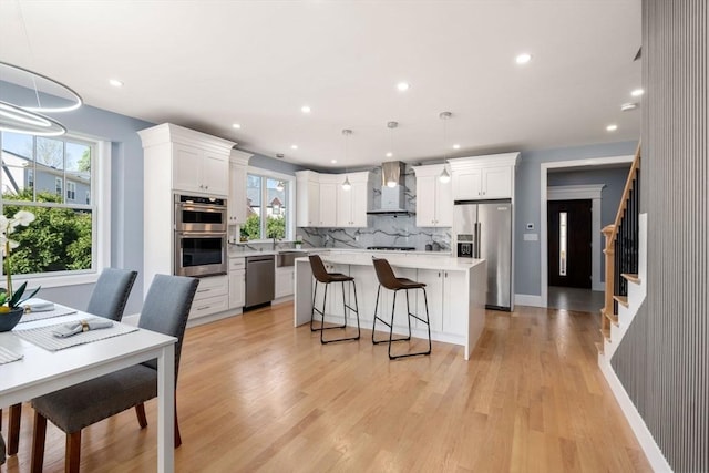 kitchen featuring wall chimney range hood, decorative backsplash, appliances with stainless steel finishes, a center island, and light countertops