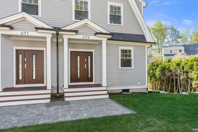 view of exterior entry featuring a lawn and roof with shingles