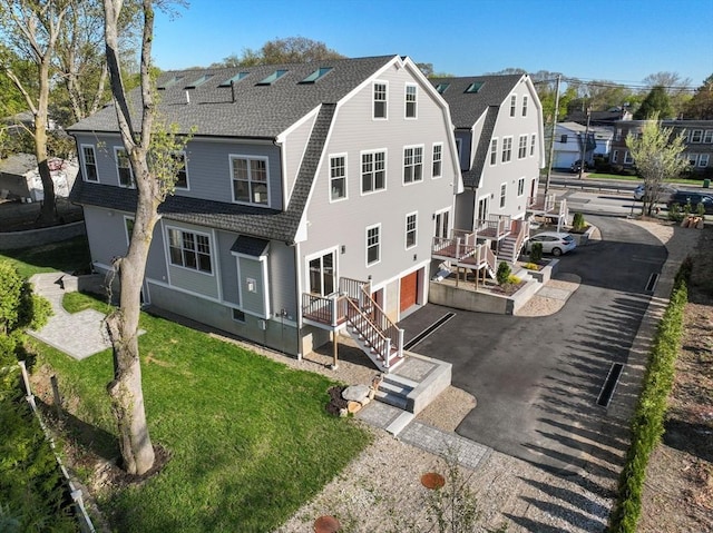 back of house with aphalt driveway, a residential view, a gambrel roof, an attached garage, and a shingled roof