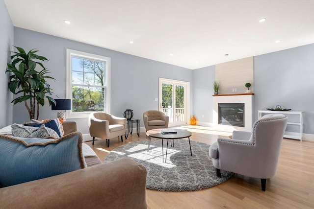 living area featuring baseboards, a glass covered fireplace, a wealth of natural light, and wood finished floors
