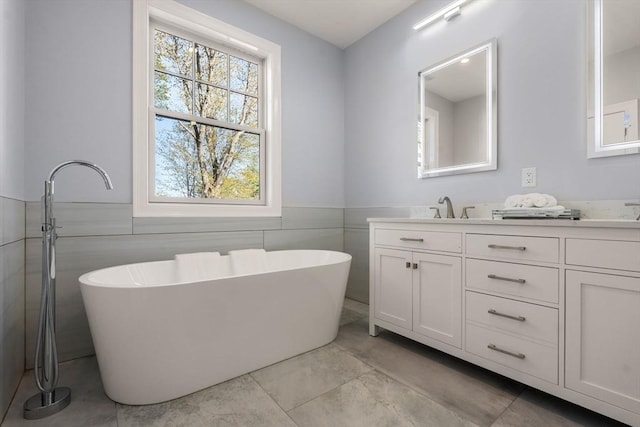 bathroom with double vanity, tile walls, a freestanding tub, wainscoting, and a sink