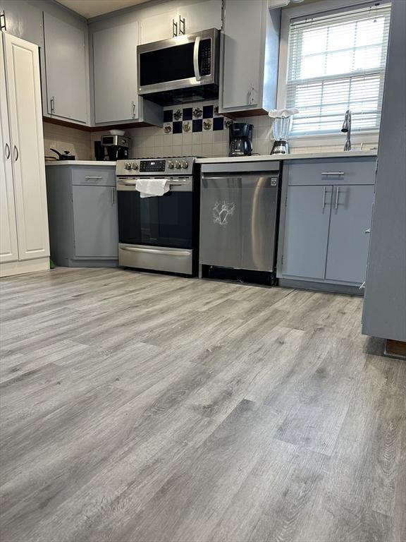 kitchen with gray cabinetry, light wood-style flooring, backsplash, stainless steel appliances, and light countertops