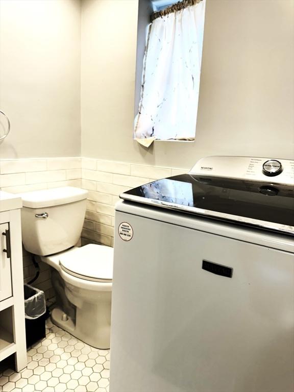 bathroom with tile patterned flooring, a wainscoted wall, toilet, washer / dryer, and tile walls