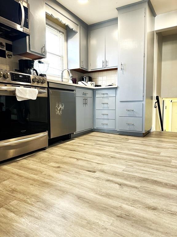 kitchen with tasteful backsplash, gray cabinets, appliances with stainless steel finishes, and light wood-type flooring