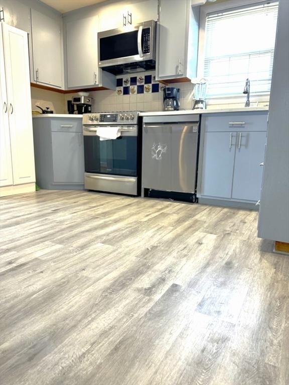 kitchen featuring backsplash, light wood-type flooring, light countertops, gray cabinets, and appliances with stainless steel finishes