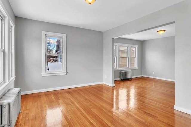 empty room featuring a healthy amount of sunlight, light wood finished floors, and radiator heating unit