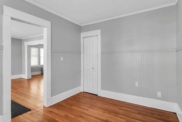 empty room with wainscoting, crown molding, and hardwood / wood-style flooring