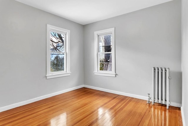 empty room with a healthy amount of sunlight, radiator heating unit, light wood-style floors, and baseboards