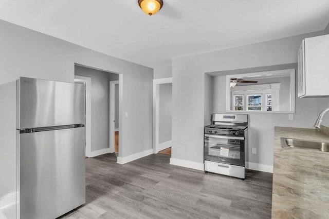 kitchen with stainless steel appliances, light countertops, white cabinetry, a sink, and wood finished floors