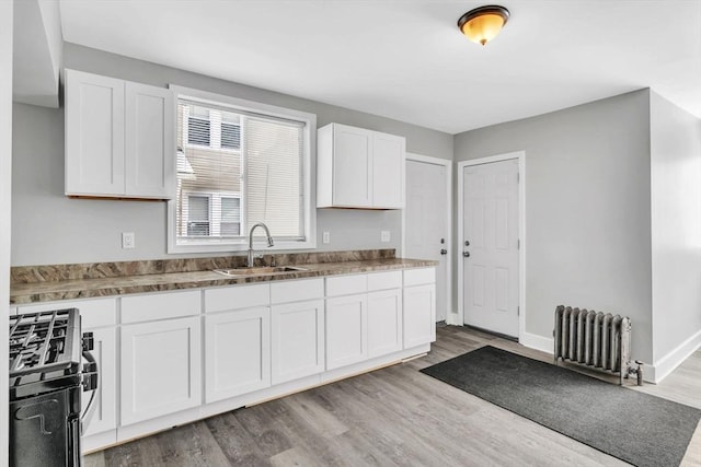 kitchen with wood finished floors, a sink, white cabinets, radiator, and gas range