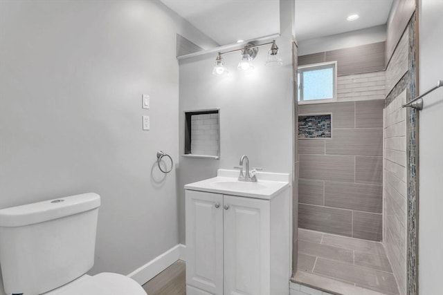 bathroom featuring tiled shower, vanity, toilet, and baseboards