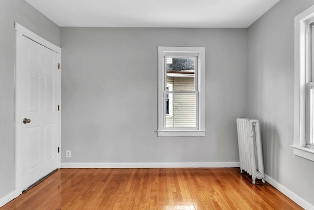 unfurnished room featuring radiator heating unit, baseboards, and wood finished floors