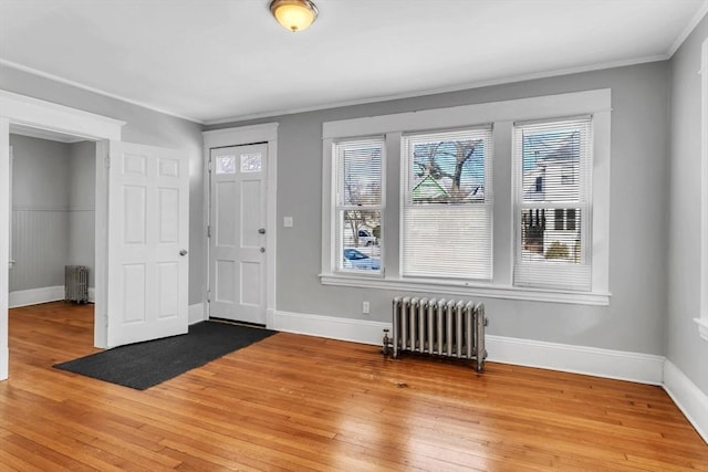 foyer featuring light wood-style floors, radiator, crown molding, and baseboards