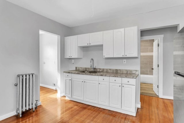 kitchen with light wood-type flooring, radiator, white cabinets, and a sink