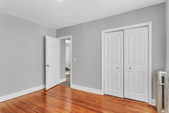 unfurnished bedroom featuring radiator heating unit, light wood-type flooring, a closet, and baseboards