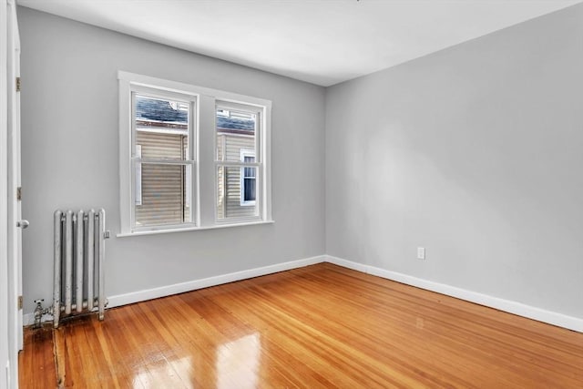 empty room with baseboards, radiator heating unit, and hardwood / wood-style flooring