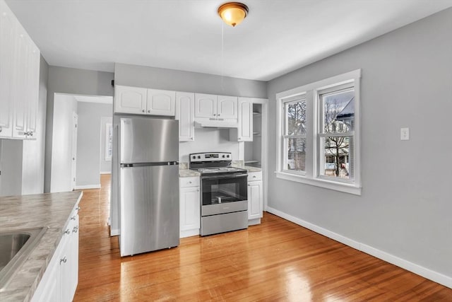 kitchen with under cabinet range hood, stainless steel appliances, baseboards, light wood-style floors, and white cabinets