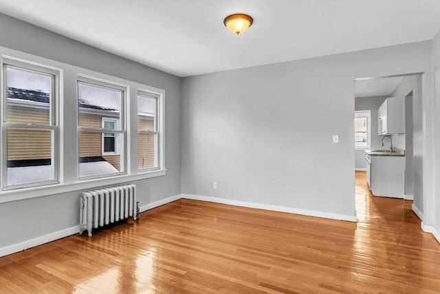 unfurnished room featuring radiator heating unit, a sink, light wood-style flooring, and baseboards