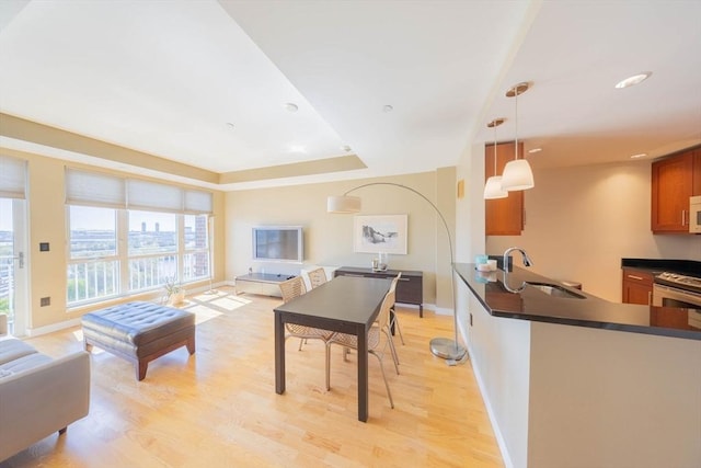 living room featuring recessed lighting, baseboards, a tray ceiling, and light wood finished floors
