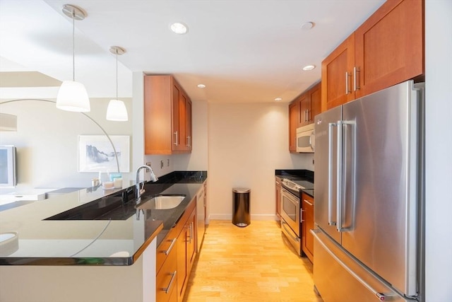 kitchen with brown cabinetry, a peninsula, light wood-type flooring, a sink, and appliances with stainless steel finishes