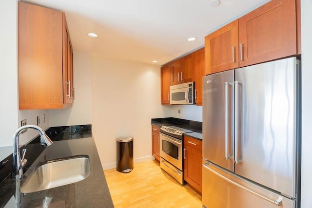 kitchen featuring brown cabinetry, light wood-style floors, a sink, dark stone countertops, and stainless steel appliances