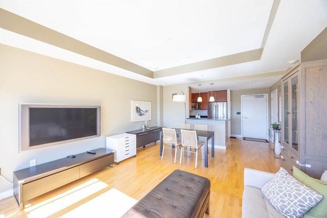 living room with a raised ceiling and light wood-style flooring