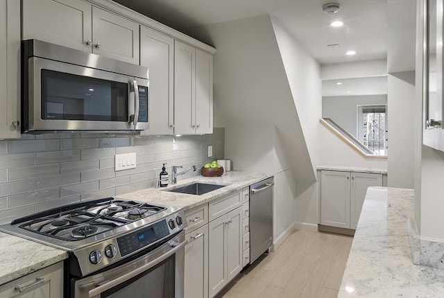 kitchen with stainless steel appliances, a sink, tasteful backsplash, light wood-style flooring, and light stone counters