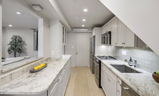 kitchen featuring appliances with stainless steel finishes, a sink, light wood-style floors, recessed lighting, and light stone counters