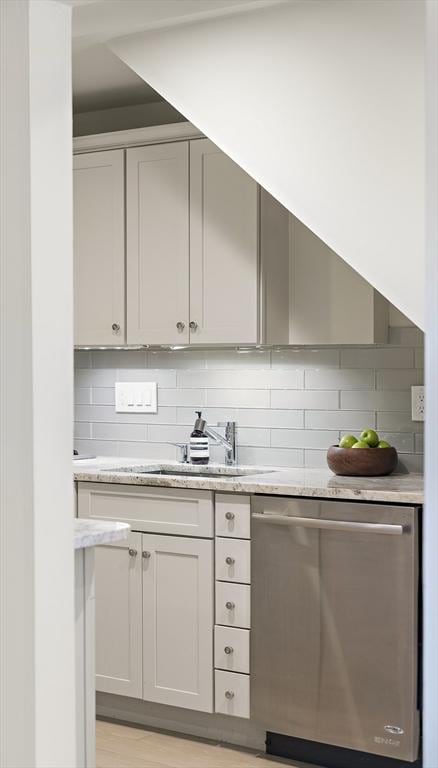 bar area featuring dishwasher, backsplash, a sink, and light wood finished floors