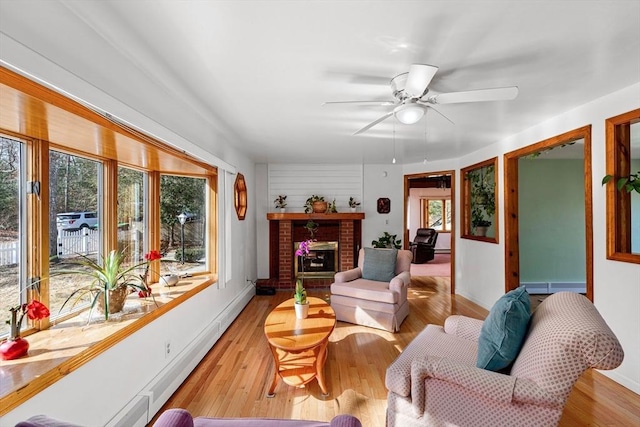 living area featuring a ceiling fan, a brick fireplace, baseboards, and light wood finished floors