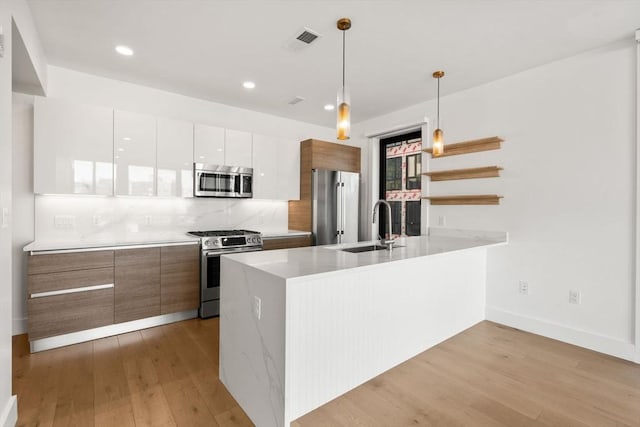 kitchen featuring appliances with stainless steel finishes, light wood-type flooring, white cabinetry, and pendant lighting