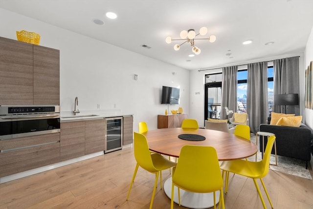 dining space featuring sink, an inviting chandelier, beverage cooler, and light wood-type flooring