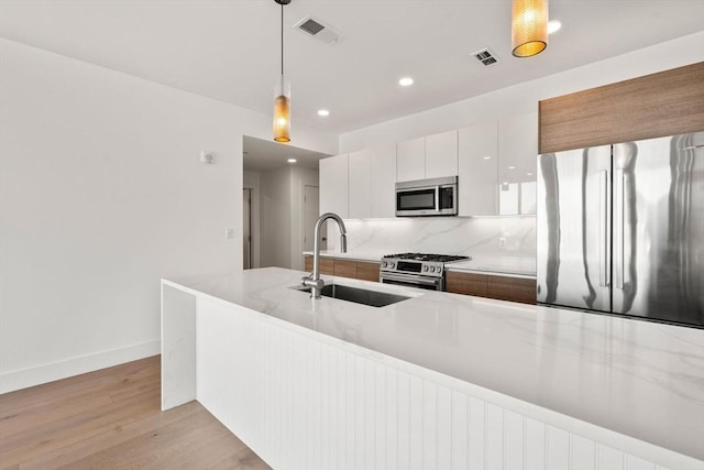 kitchen with white cabinetry, sink, light hardwood / wood-style floors, decorative light fixtures, and appliances with stainless steel finishes