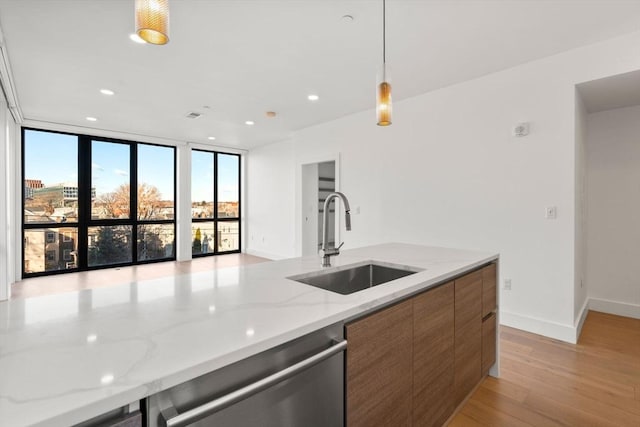 kitchen with light stone countertops, dishwasher, sink, light hardwood / wood-style flooring, and pendant lighting