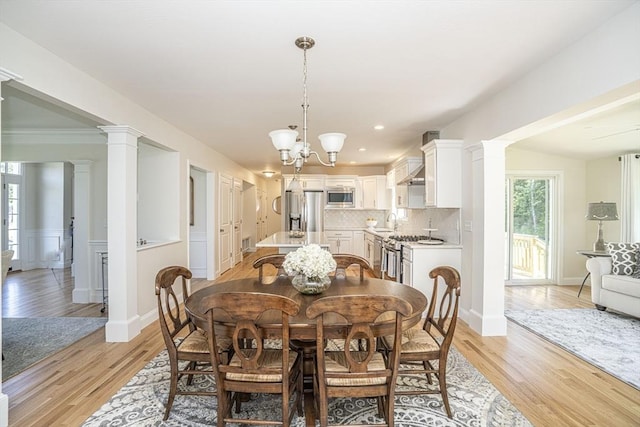 dining room with an inviting chandelier, sink, light hardwood / wood-style flooring, and decorative columns