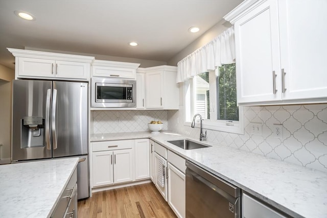 kitchen with light wood-type flooring, stainless steel appliances, white cabinetry, and sink