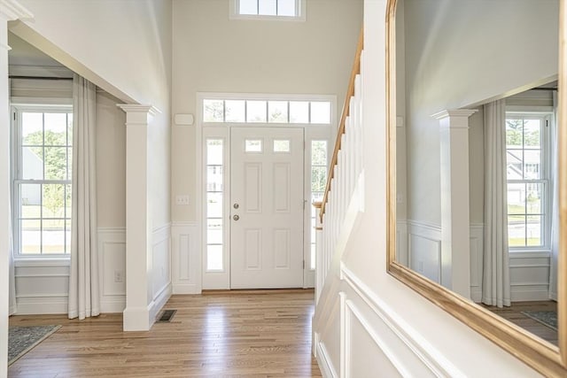 foyer entrance featuring light hardwood / wood-style flooring, ornate columns, and a healthy amount of sunlight