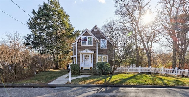 shingle-style home featuring fence and a front lawn