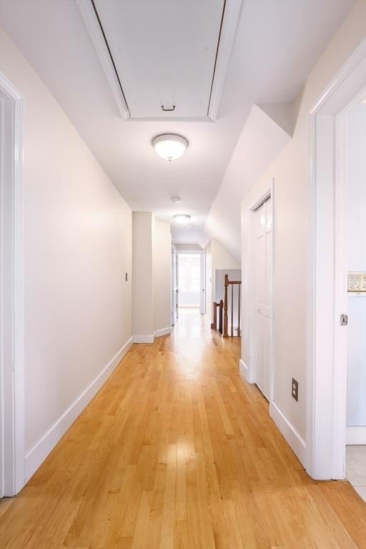 hall featuring attic access, baseboards, lofted ceiling, light wood-style flooring, and an upstairs landing