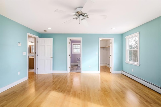 unfurnished bedroom featuring a baseboard radiator, light wood-style flooring, baseboards, and a spacious closet