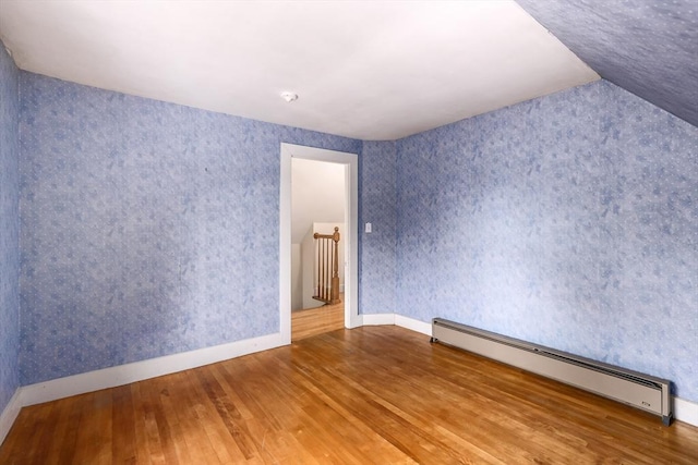 unfurnished room featuring a baseboard heating unit, wallpapered walls, baseboards, and wood finished floors