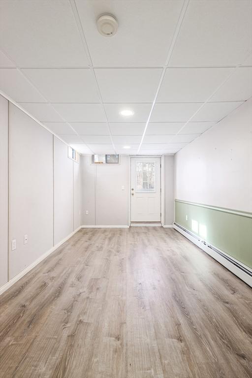 below grade area featuring a paneled ceiling, a baseboard radiator, and wood finished floors