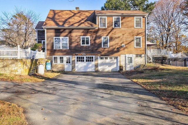 view of front of house featuring aphalt driveway, a chimney, an attached garage, and fence