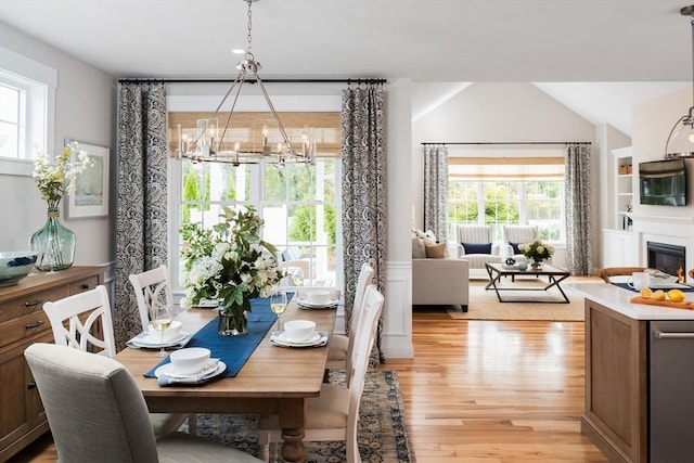 dining room with light hardwood / wood-style flooring, vaulted ceiling, and a notable chandelier