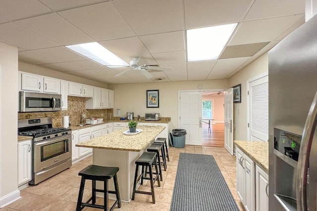 kitchen featuring white cabinetry, a center island, stainless steel appliances, a kitchen bar, and decorative backsplash