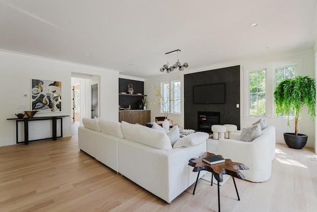 living room featuring a notable chandelier, crown molding, a fireplace, and light hardwood / wood-style floors